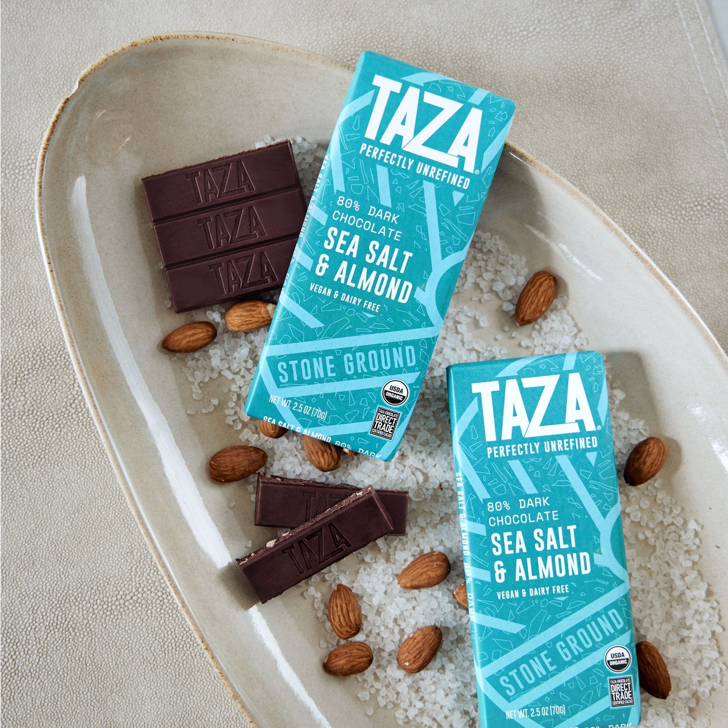 Wrapped and unwrapped Sea Salt & Almond Bar, lying in a bed of salt and almonds.