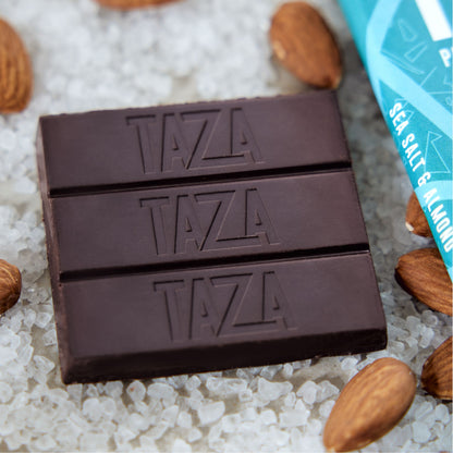 Close up shot of an unwrapped Sea Salt & Almond Bar lying in a bed of salt and almonds.